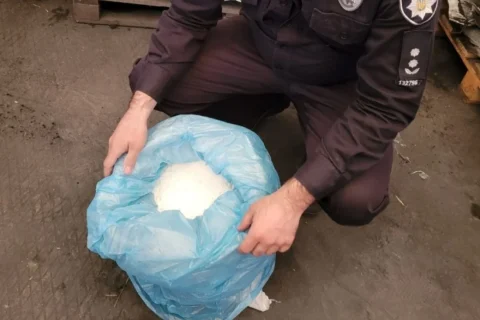 Поліцейський тримає в руках синій пакет з вилученим наркотиком на асфальті